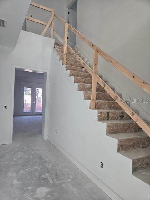 stairway featuring french doors and concrete flooring