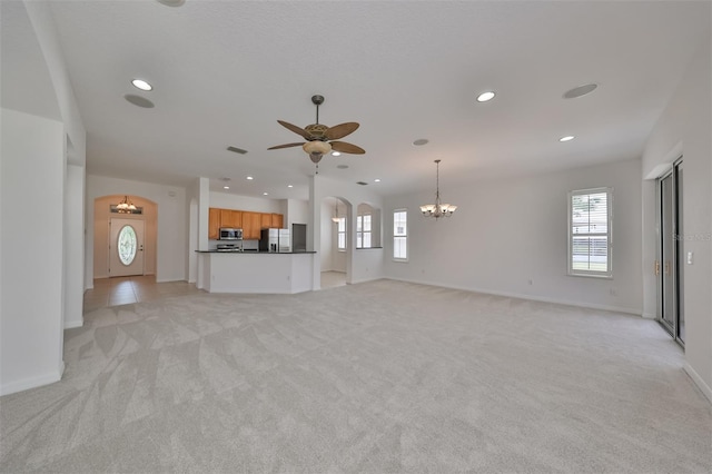 unfurnished living room featuring ceiling fan with notable chandelier and light colored carpet