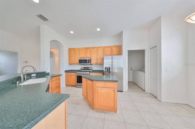 kitchen with a center island, washing machine and dryer, appliances with stainless steel finishes, sink, and light tile floors