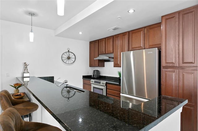 kitchen with dark stone counters, stainless steel appliances, a kitchen breakfast bar, hanging light fixtures, and sink