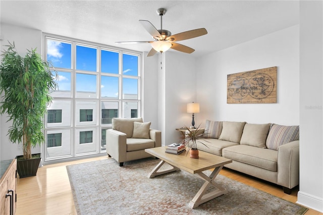 living room featuring ceiling fan, a textured ceiling, light hardwood / wood-style flooring, and a wall of windows