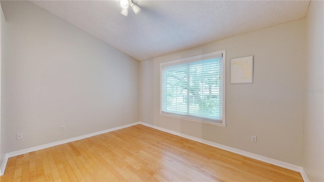 spare room with vaulted ceiling, a textured ceiling, and light wood-type flooring