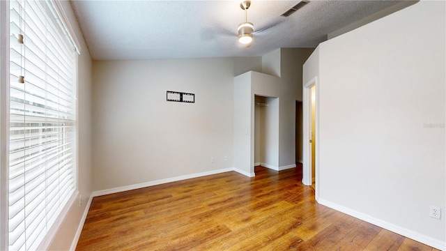 spare room with a wealth of natural light, ceiling fan, vaulted ceiling, and light wood-type flooring