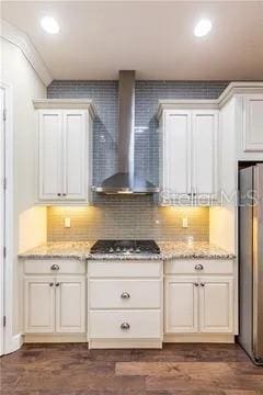 kitchen with light stone counters, fridge, white cabinetry, wall chimney range hood, and stainless steel gas stovetop