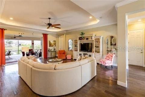 living room with ceiling fan, a tray ceiling, and dark hardwood / wood-style floors