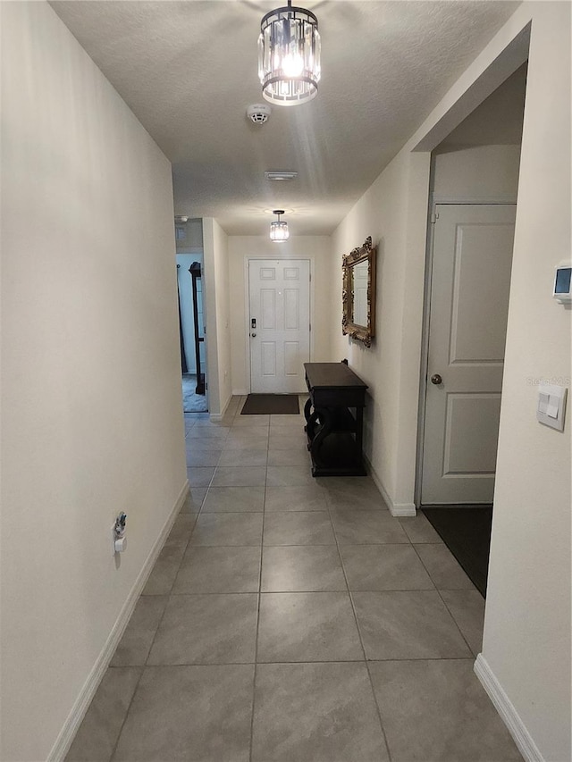 hall featuring a textured ceiling, light tile patterned floors, and a notable chandelier