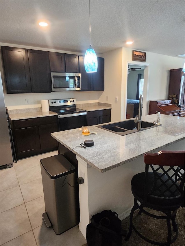 kitchen with light tile patterned floors, stainless steel appliances, sink, light stone countertops, and hanging light fixtures