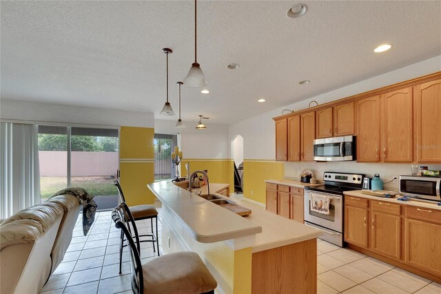 kitchen featuring a kitchen island, stainless steel appliances, a kitchen breakfast bar, hanging light fixtures, and sink