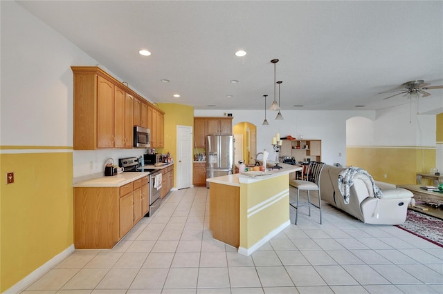 kitchen featuring a kitchen breakfast bar, stainless steel appliances, an island with sink, ceiling fan, and light tile floors