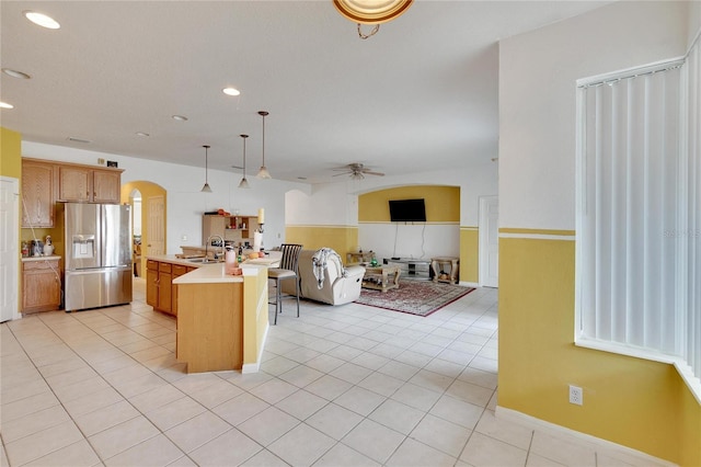 kitchen with pendant lighting, light tile floors, sink, a kitchen island with sink, and stainless steel fridge with ice dispenser