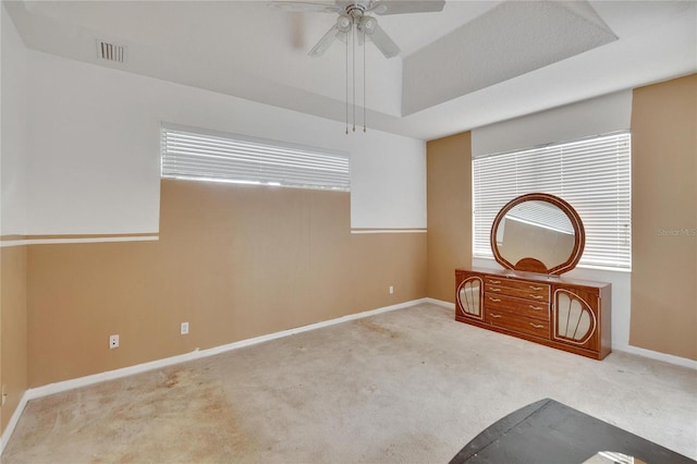 interior space featuring a tray ceiling, carpet floors, multiple windows, and ceiling fan