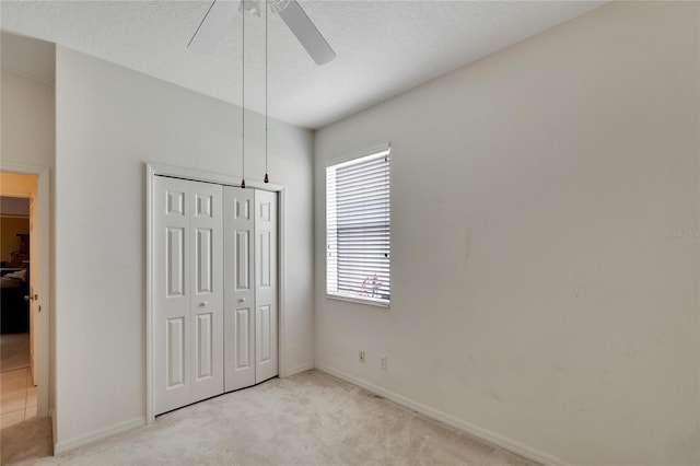 unfurnished bedroom featuring light carpet, a closet, ceiling fan, and a textured ceiling