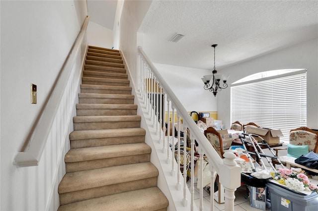 stairs with a textured ceiling, light tile floors, and a chandelier