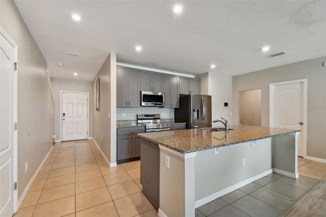 kitchen featuring dark stone countertops, appliances with stainless steel finishes, a kitchen island with sink, and gray cabinetry