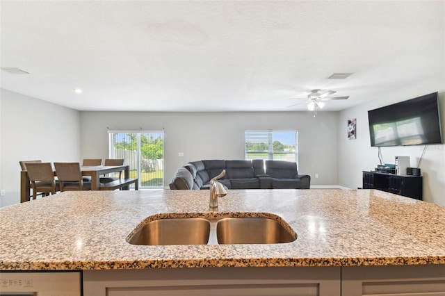 kitchen featuring an island with sink, sink, a wealth of natural light, and light stone counters