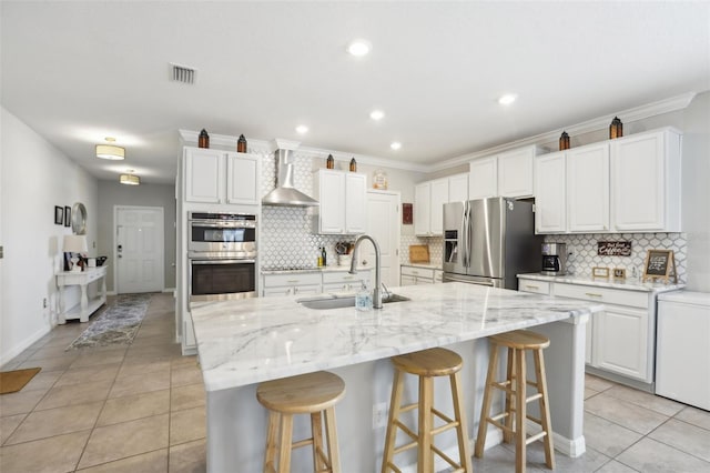 kitchen featuring a center island with sink, wall chimney range hood, tasteful backsplash, and appliances with stainless steel finishes