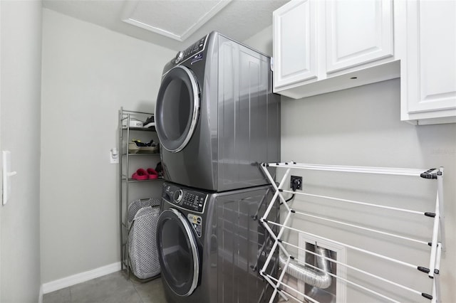 clothes washing area with stacked washer and clothes dryer, cabinets, and light tile floors