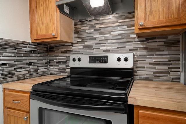 kitchen with wall chimney exhaust hood, decorative backsplash, stainless steel range with electric cooktop, and butcher block counters