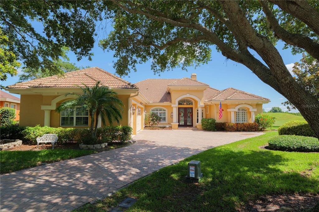 mediterranean / spanish home with a tiled roof, french doors, decorative driveway, a chimney, and a front yard