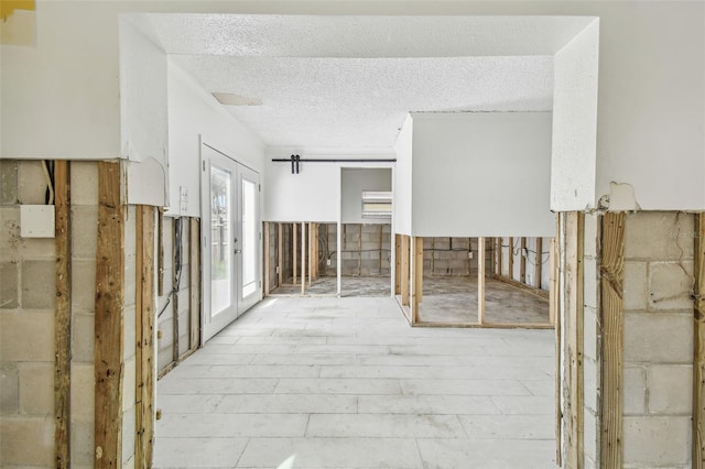 hallway with a barn door, a textured ceiling, and french doors