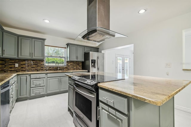 kitchen with french doors, a kitchen island, appliances with stainless steel finishes, island range hood, and light stone counters