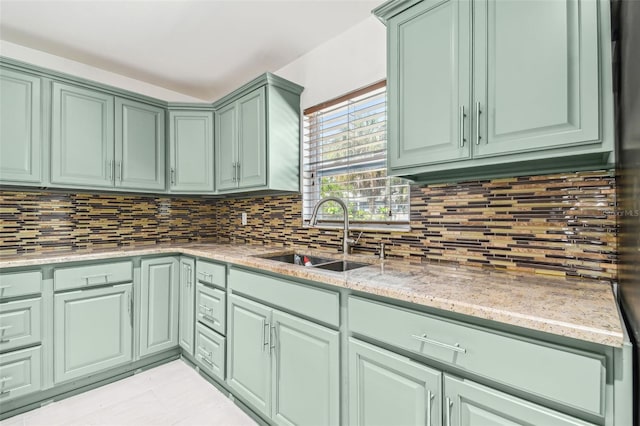 kitchen with backsplash, light stone counters, green cabinets, and sink