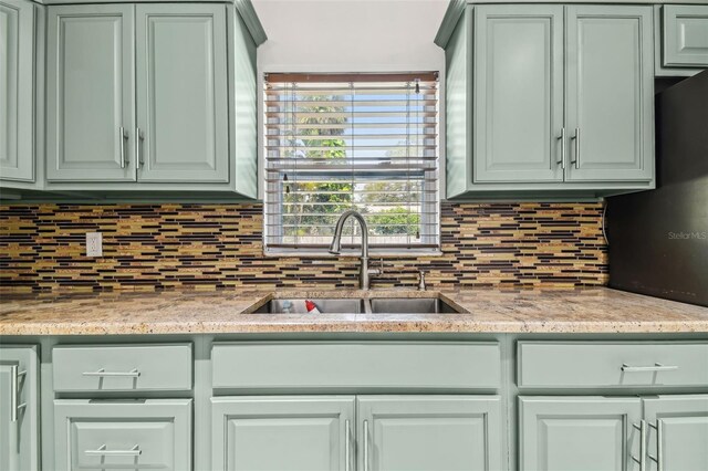 kitchen featuring decorative backsplash, light stone counters, and sink