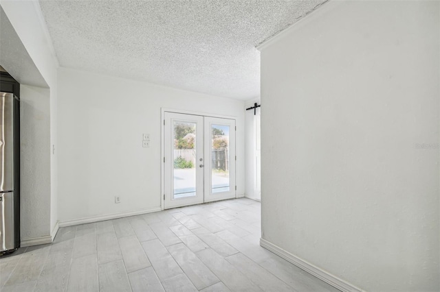 unfurnished room with light hardwood / wood-style flooring, a barn door, a textured ceiling, and french doors