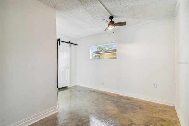 spare room with a textured ceiling, a barn door, concrete floors, and ceiling fan