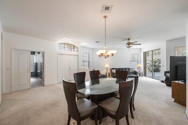 dining space with ceiling fan with notable chandelier and light colored carpet