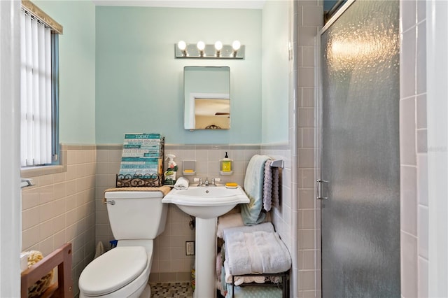 bathroom featuring toilet, a shower with shower door, and tile walls