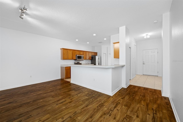 kitchen with a textured ceiling, appliances with stainless steel finishes, wood-type flooring, rail lighting, and sink