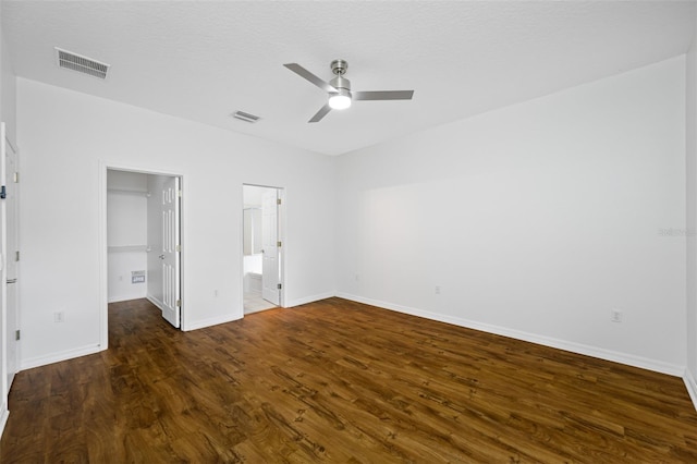 unfurnished bedroom featuring a walk in closet, dark wood-type flooring, ensuite bathroom, and ceiling fan