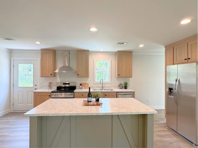 kitchen with wall chimney range hood, a kitchen island, light wood-type flooring, appliances with stainless steel finishes, and sink