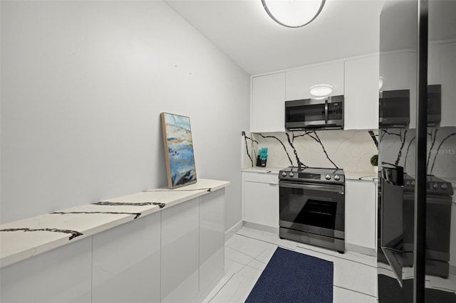 kitchen with white cabinetry, light stone countertops, appliances with stainless steel finishes, backsplash, and light tile floors