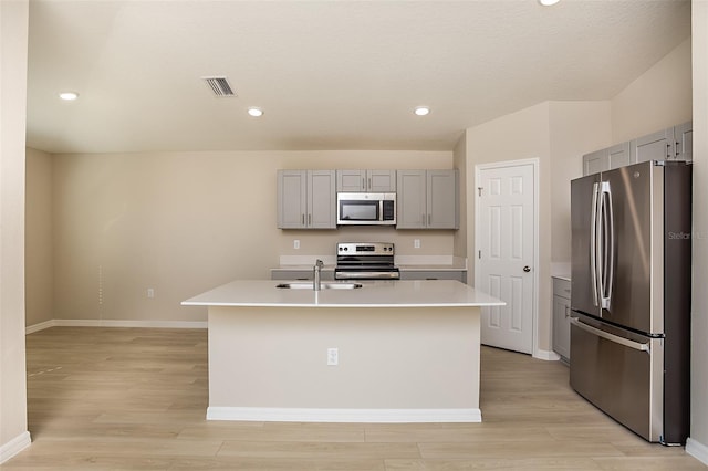 kitchen with light hardwood / wood-style flooring, stainless steel appliances, a center island with sink, gray cabinets, and sink