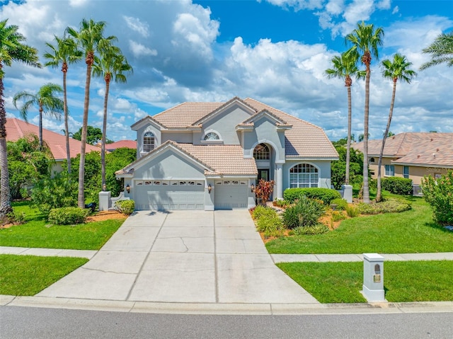 mediterranean / spanish home with stucco siding, an attached garage, driveway, a tiled roof, and a front lawn