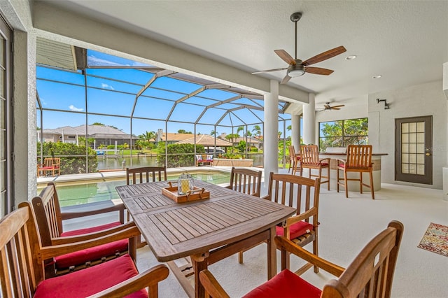 view of patio featuring ceiling fan, a water view, and glass enclosure