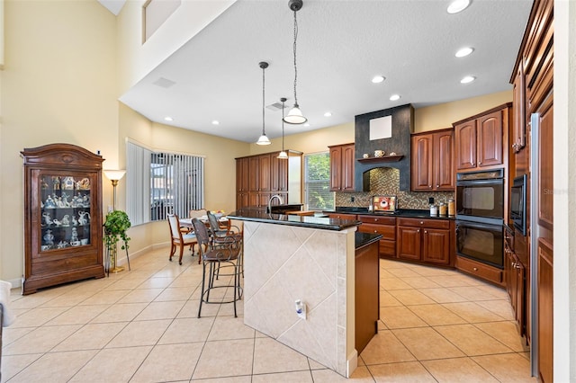 kitchen with decorative backsplash, light tile patterned floors, hanging light fixtures, a breakfast bar area, and an island with sink