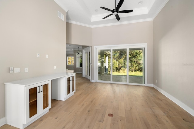 unfurnished living room with ceiling fan, a raised ceiling, plenty of natural light, and light wood-type flooring