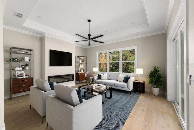 living room featuring ceiling fan, light hardwood / wood-style floors, a raised ceiling, and crown molding