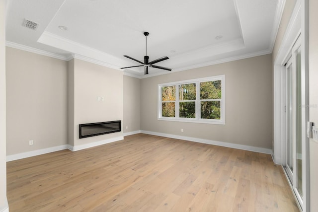 unfurnished living room featuring a tray ceiling, ceiling fan, light hardwood / wood-style floors, and ornamental molding