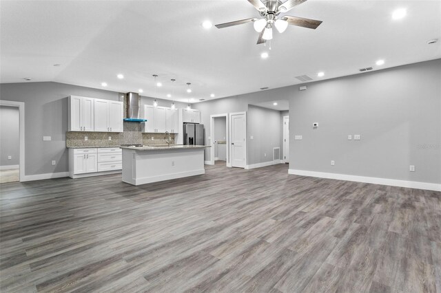 kitchen with stainless steel fridge, a kitchen island, pendant lighting, wall chimney range hood, and white cabinets