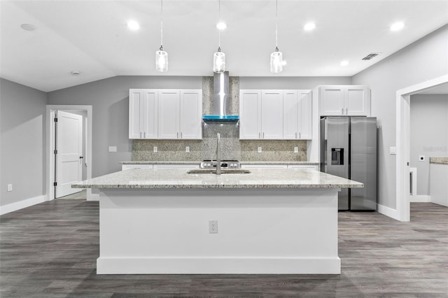 kitchen featuring a kitchen island with sink, stainless steel refrigerator with ice dispenser, light stone counters, white cabinets, and wall chimney exhaust hood