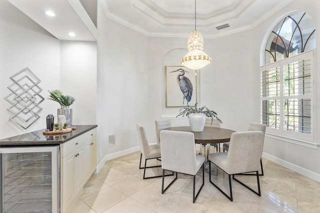 dining area featuring an inviting chandelier, beverage cooler, a raised ceiling, and ornamental molding