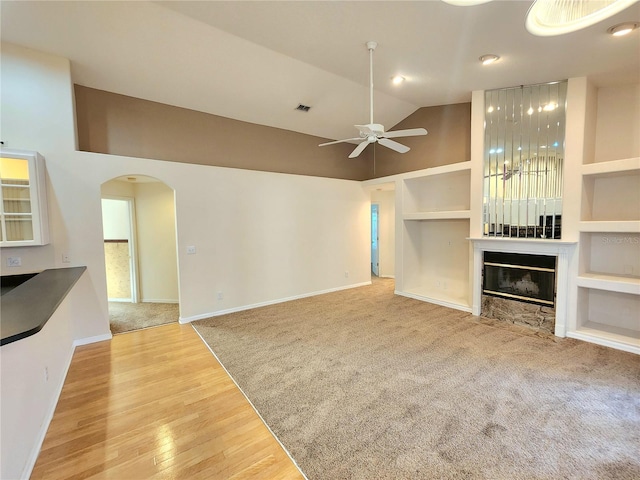 unfurnished living room with vaulted ceiling, built in shelves, ceiling fan, and light wood-type flooring