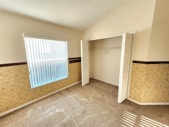 unfurnished bedroom with carpet, a closet, a textured ceiling, and lofted ceiling