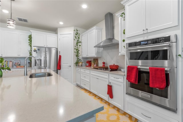 kitchen featuring decorative backsplash, wall chimney exhaust hood, stainless steel appliances, sink, and white cabinetry