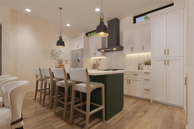 kitchen featuring decorative light fixtures, white cabinets, stainless steel built in fridge, and wall chimney exhaust hood