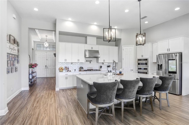 kitchen featuring hardwood / wood-style floors, a center island with sink, a towering ceiling, sink, and appliances with stainless steel finishes